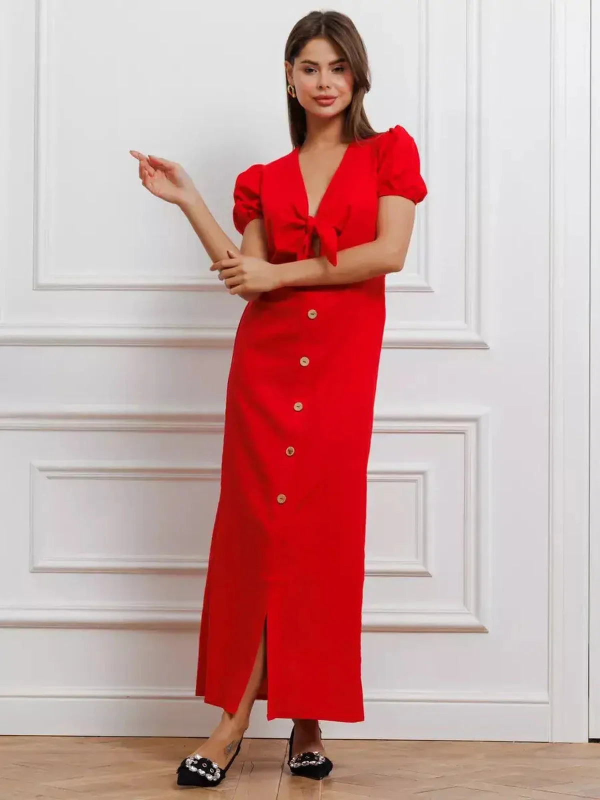 Model wearing a red maxi dress with a tie-front, puff sleeves, and button-down skirt, showcasing bold elegance.