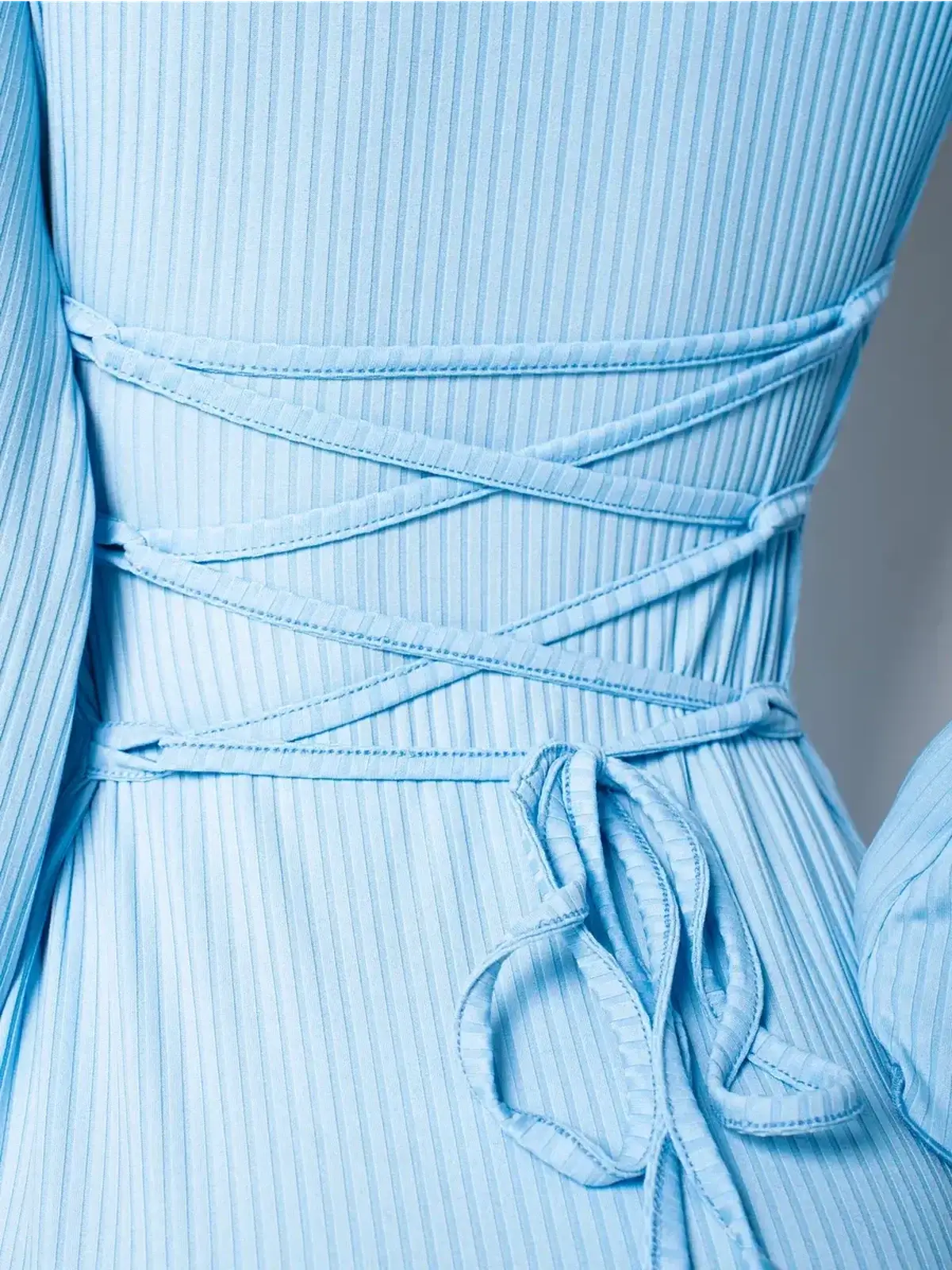 Close-up of the lace-up back detail on a light blue midi dress with ribbed fabric and long bell sleeves.
