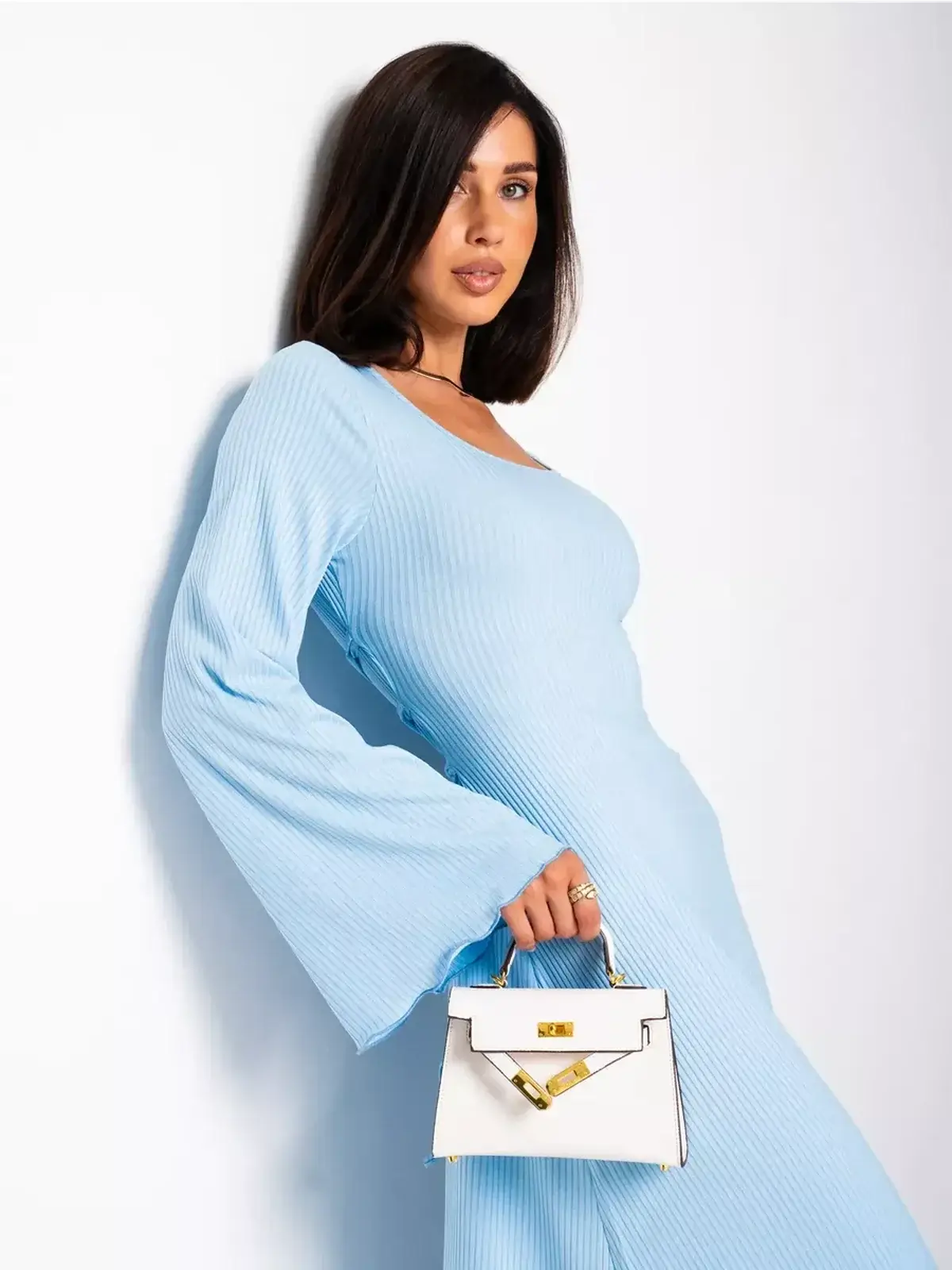 Model wearing a light blue ribbed midi dress with bell sleeves, holding a stylish white handbag.