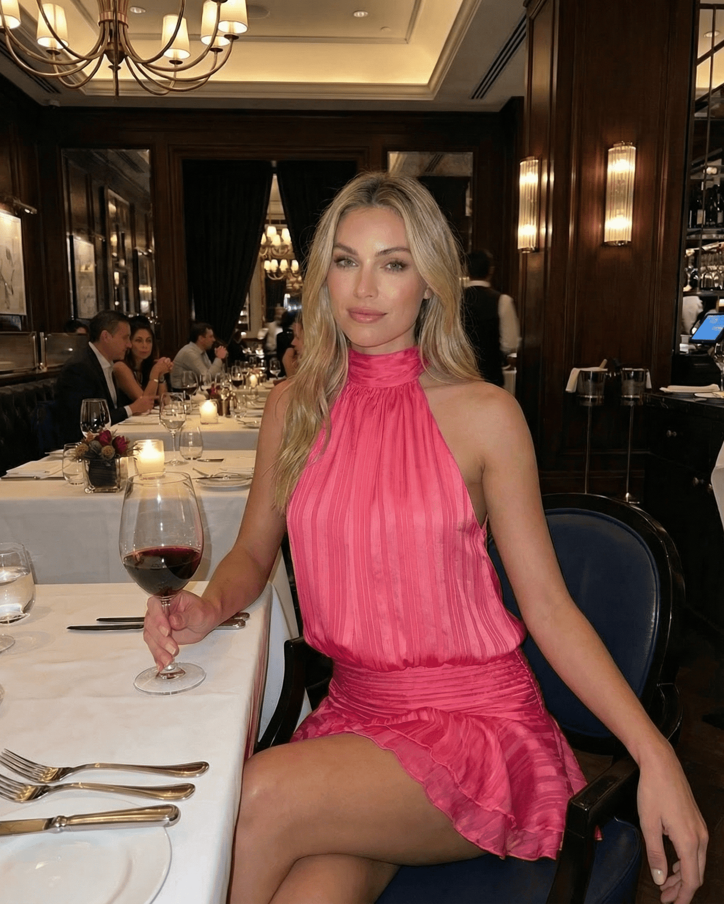 Woman enjoying dinner in a restaurant wearing the Roselle Mini Dress by Lauven, featuring a pleated design and halter neckline.
