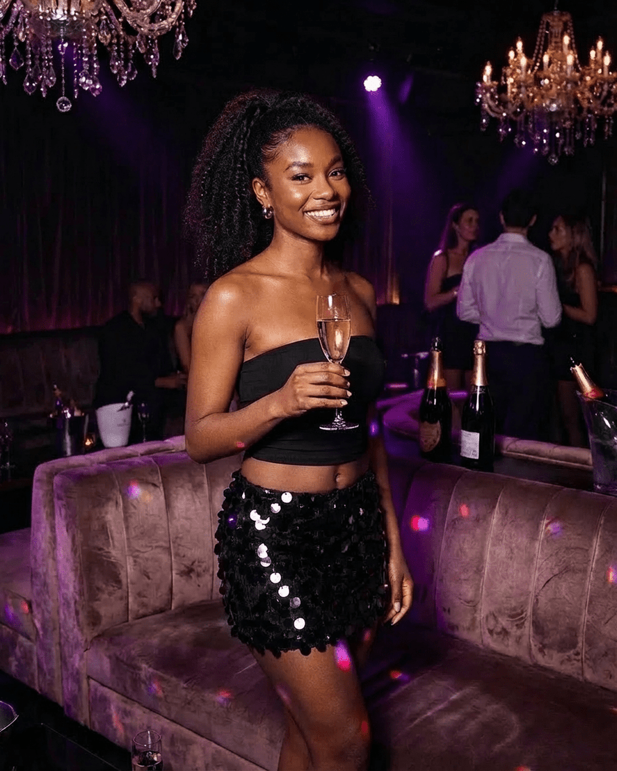 Woman wearing a Noir Mini Skirt by Lauven, black sequined A-line bodycon mini skirt, holding a champagne glass in a chic lounge.