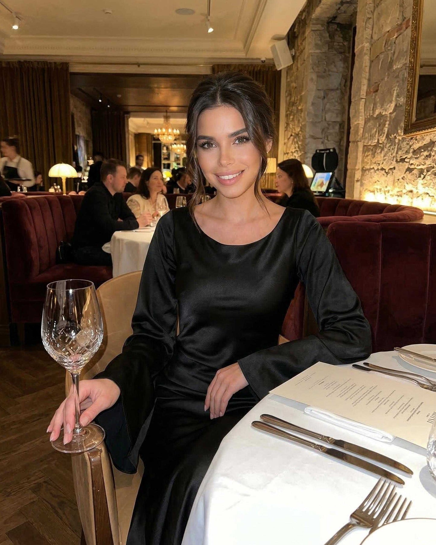 Liora Maxi Dress by Lauven elegantly worn in a dining setting, featuring bell sleeves and luxurious satin fabric.