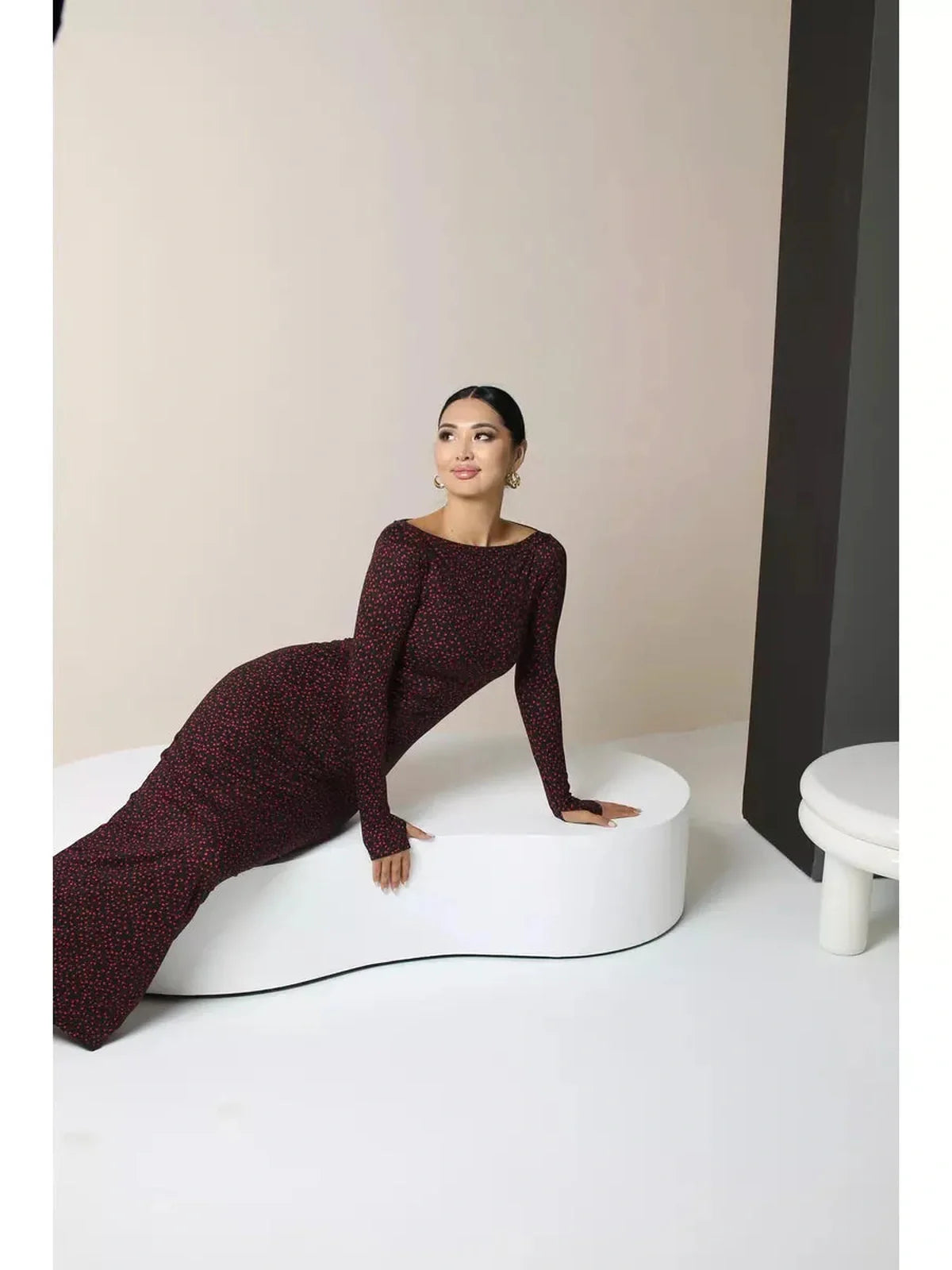 Elegant woman in a black bodycon maxi dress with heart print, posing on a stylish white sculpture.