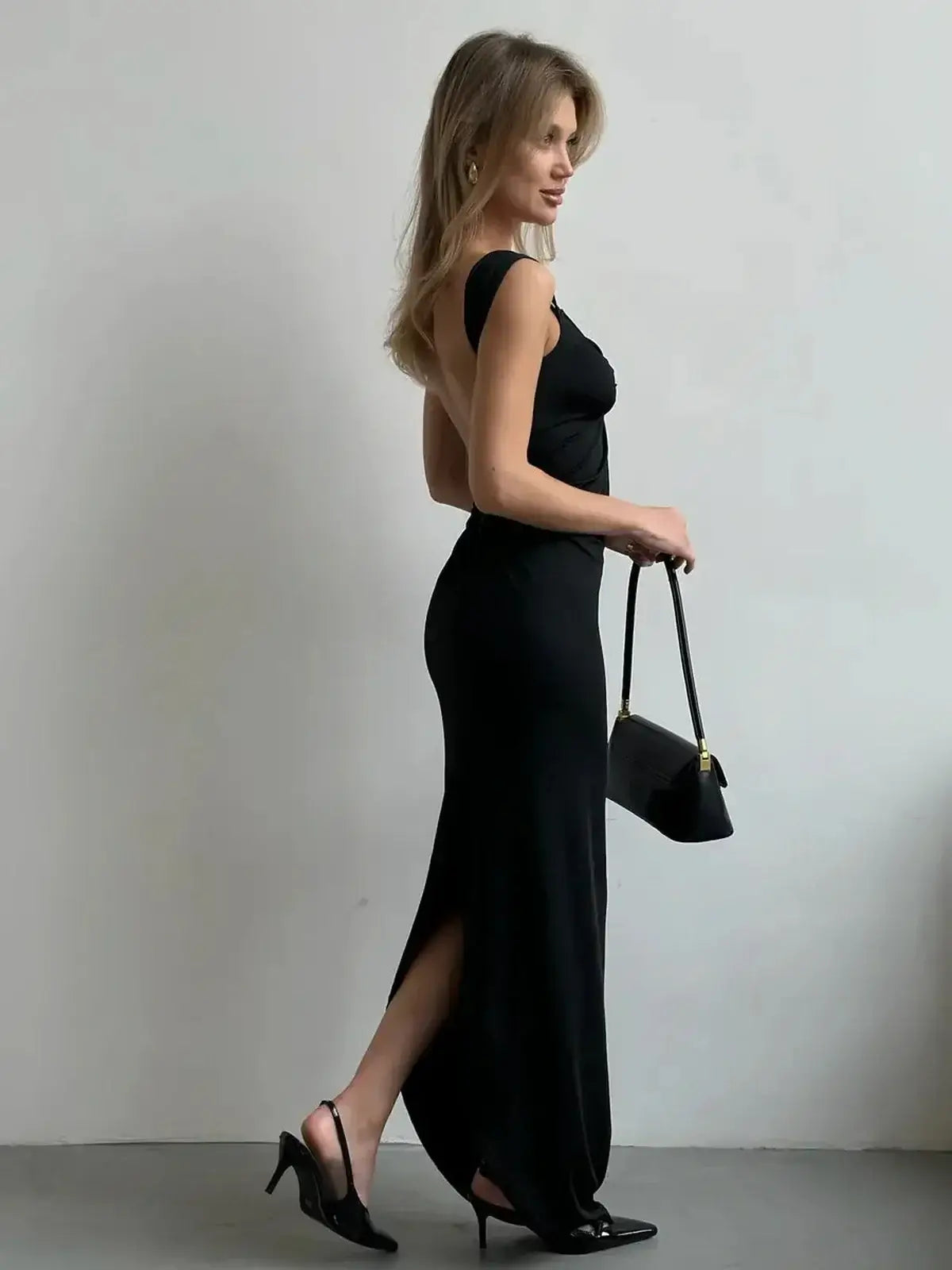 Model showcasing the Maxi Dress Obsidian Charm with a plunging neckline and thigh-high slit, paired with a chic handbag.