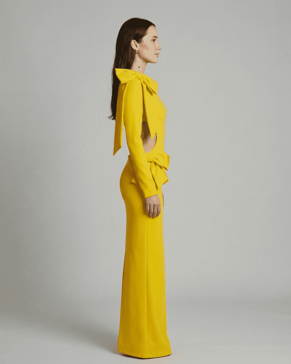 Solara Maxi Dress by Lauven featuring a side view of a yellow long sleeve bodycon design with cut-out waist and bows.