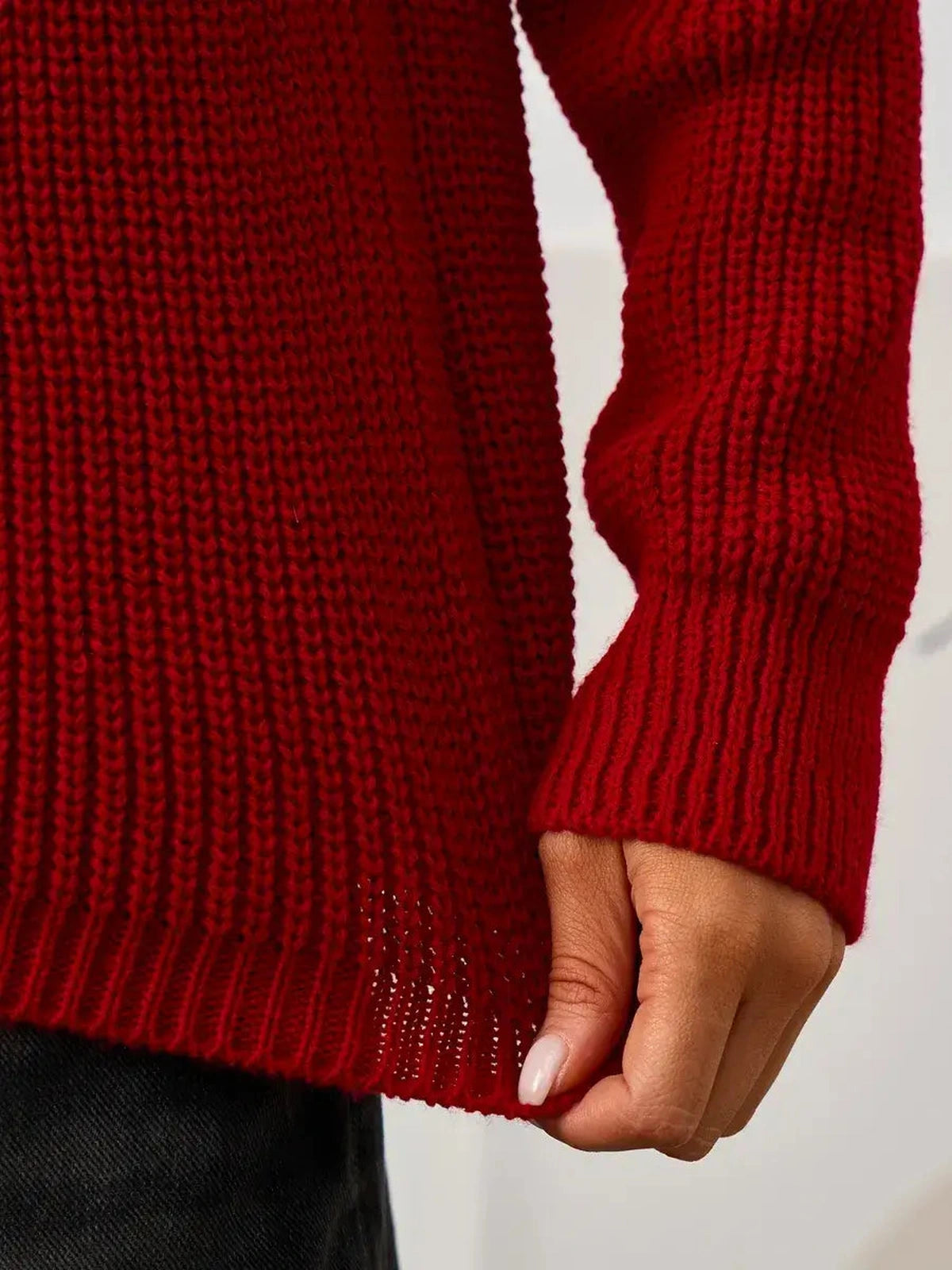 Detail shot of woman holding the hem of the Solara Sweater by Lauven, showcasing its rich red knit texture.