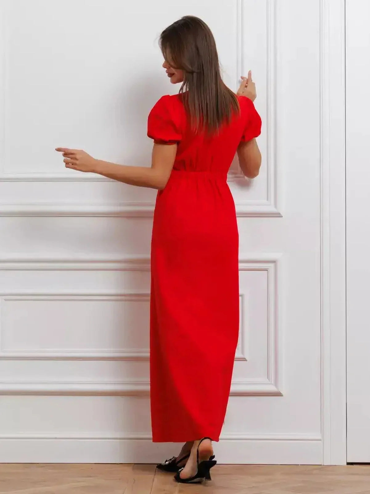 Back view of a woman in a bold red maxi dress featuring puff sleeves and a tie-front detail, exuding elegance.