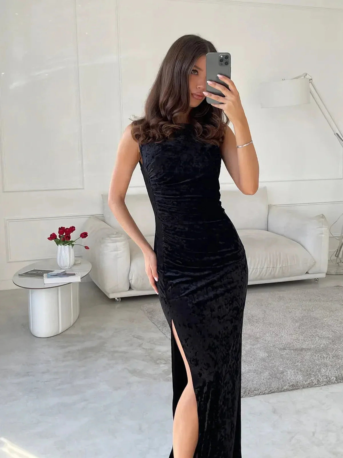 Model showcasing the Noir Muse Maxi Dress, a black velvet gown featuring a thigh-high slit and elegant silhouette.