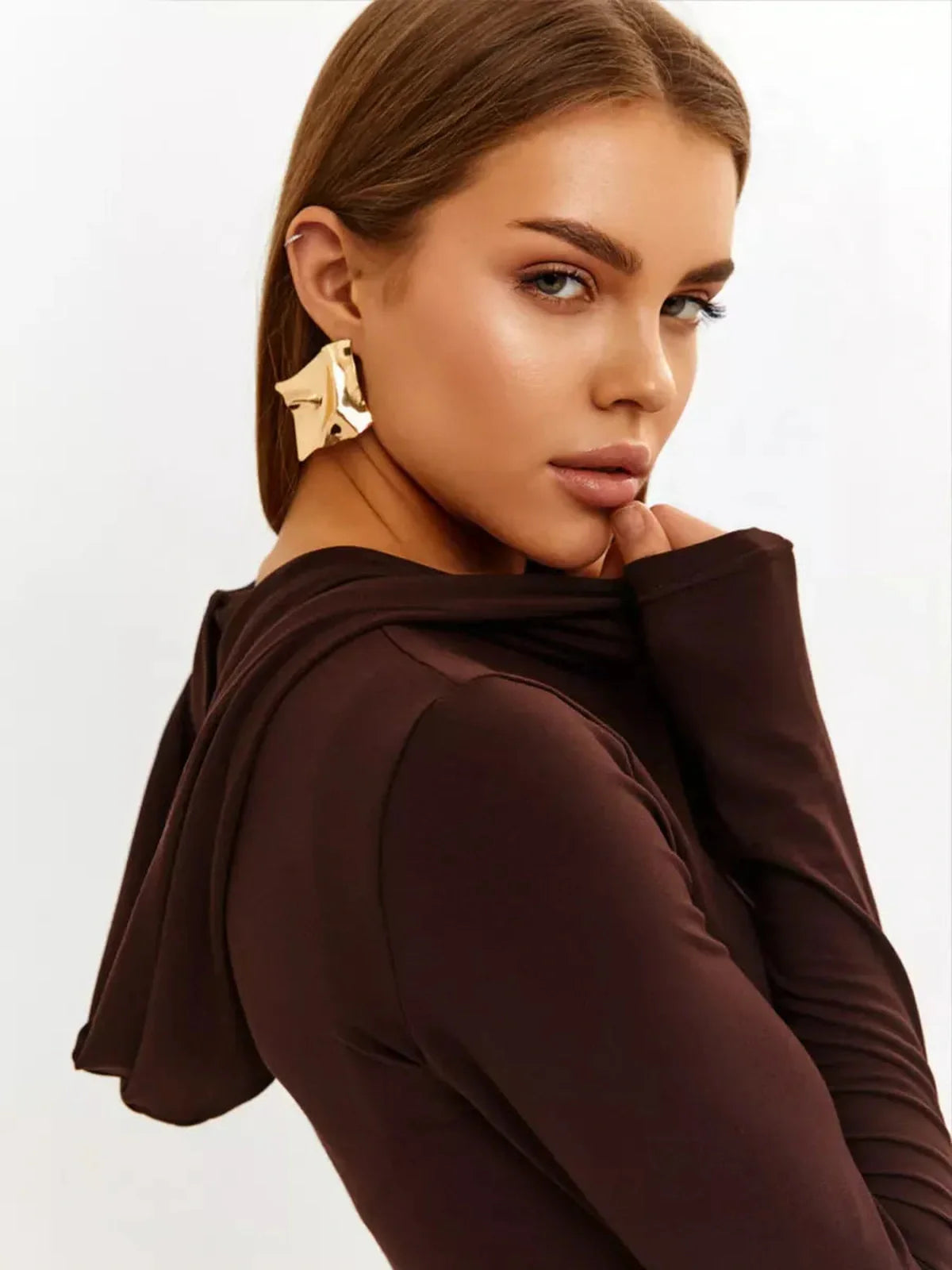 Model showcasing the Sculpt Maxi Dress in chocolate with hood detail and gold earrings, highlighting modern elegance.
