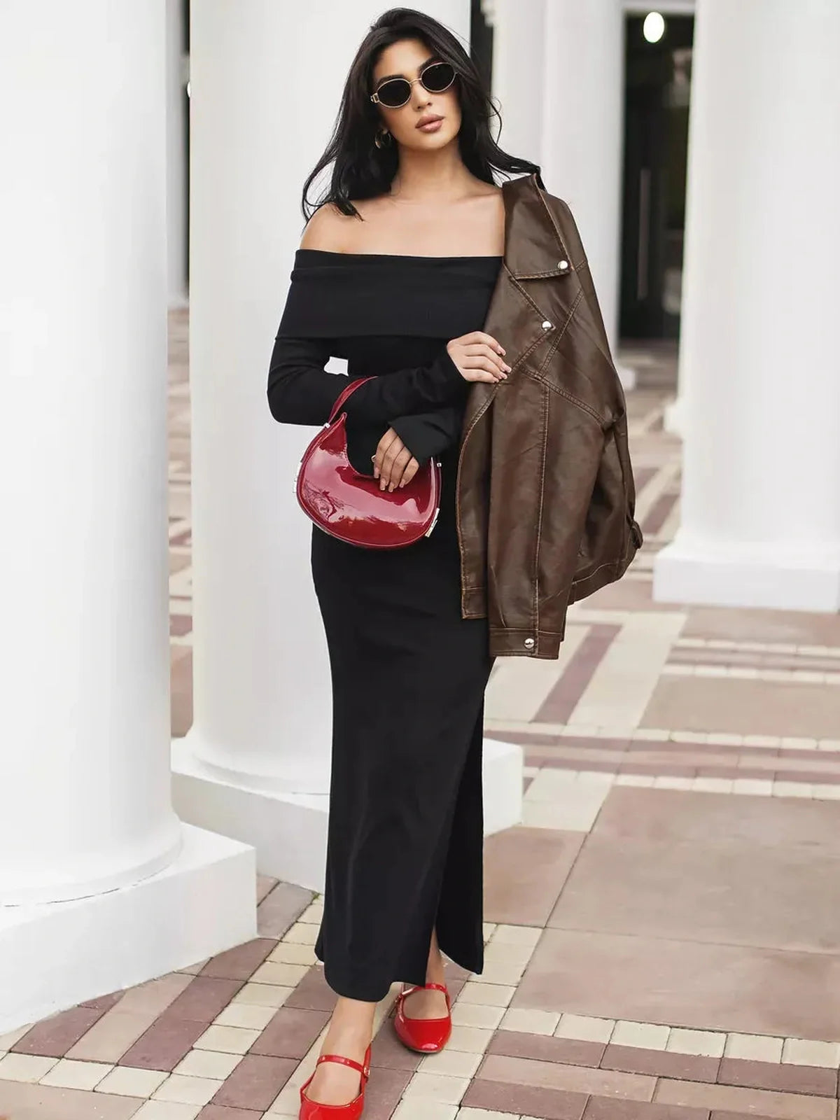 Model showcasing the Iconic Maxi Dress with off-shoulder neckline and side slit, styled with a leather jacket and red accessories.