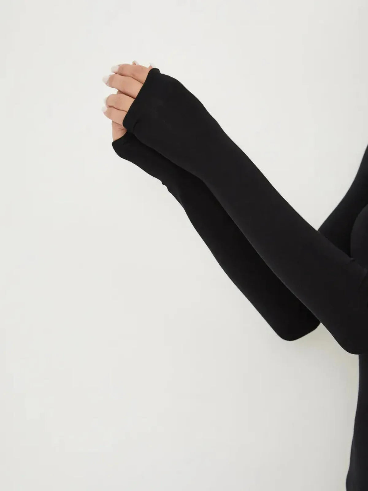 Close-up of hands in black long sleeve top with fingerless design, showcasing elegant minimalist style.