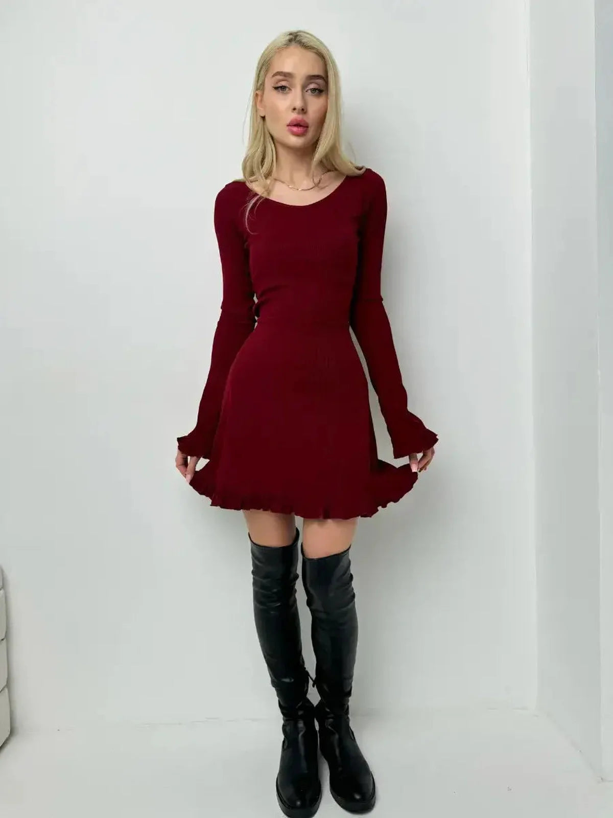 Model wearing a crimson red mini dress with romantic ruffles and fitted bodice, paired with knee-high black boots.