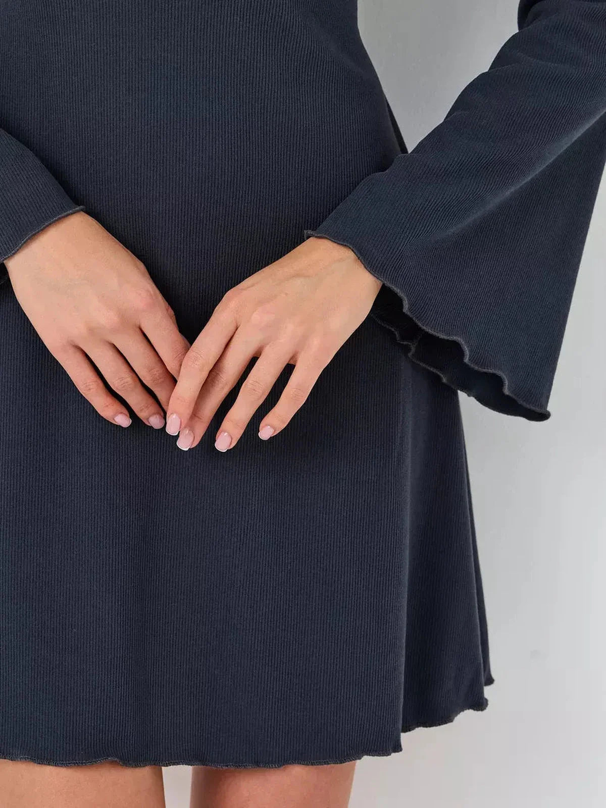 Close-up of hands on the flared sleeves and hem of the Graphite Grace mini dress, showcasing its textured fabric.