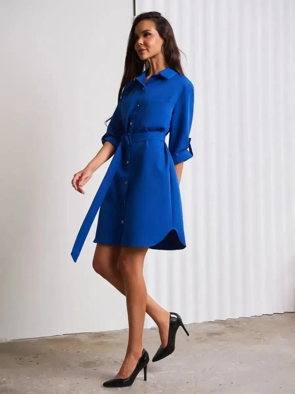 Model in a cobalt blue mini dress with a waist belt and snap-buttons, showcasing elegant structure and vibrant color.