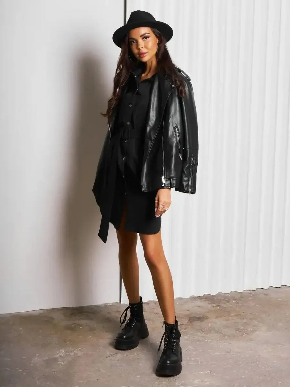 Woman in black mini dress with leather jacket, hat, and combat boots, showcasing urban chic style.
