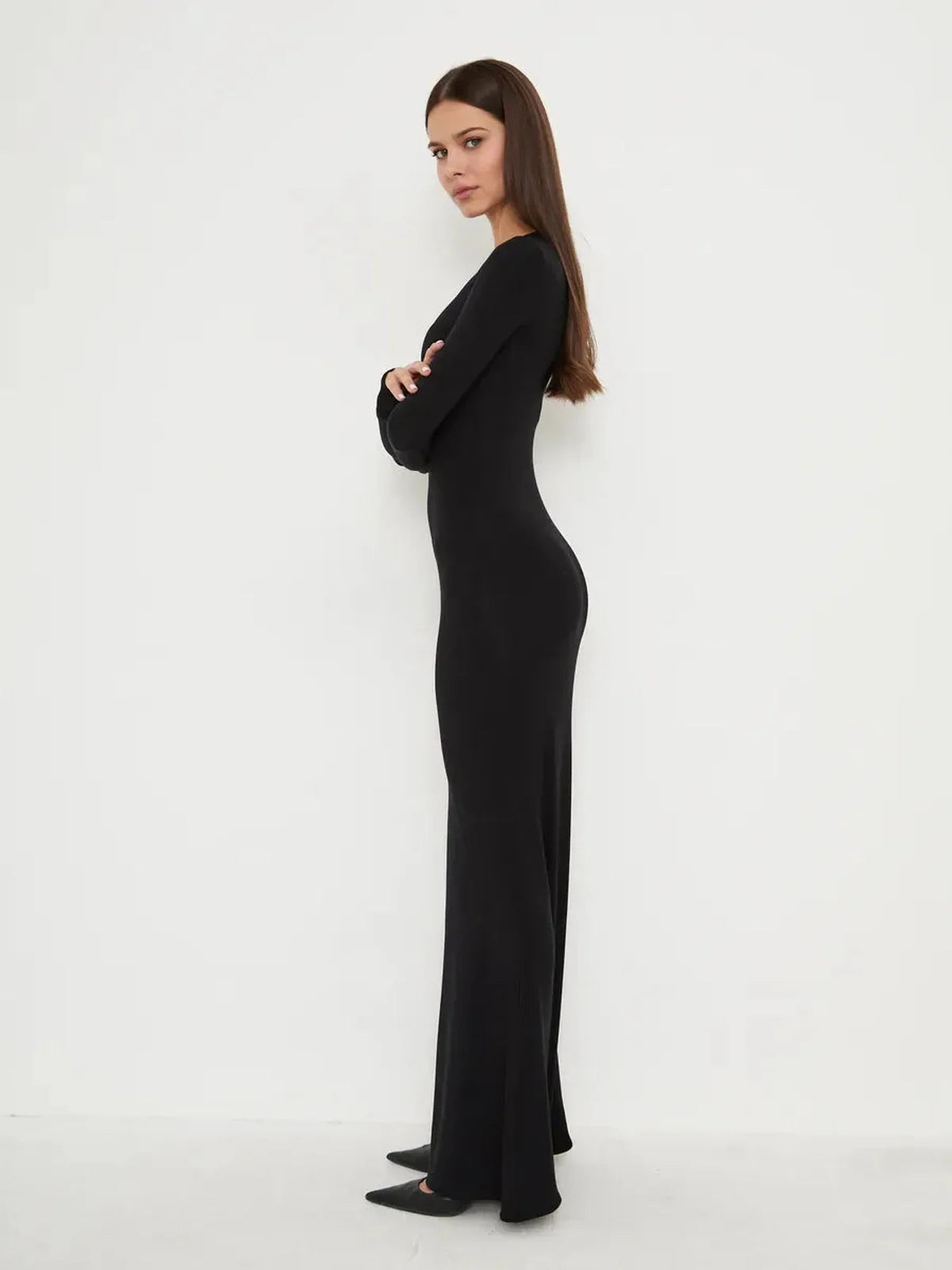 Profile view of a model in the Sculpted Noir full-length black dress, showcasing its sleek, minimal design and flattering fit.