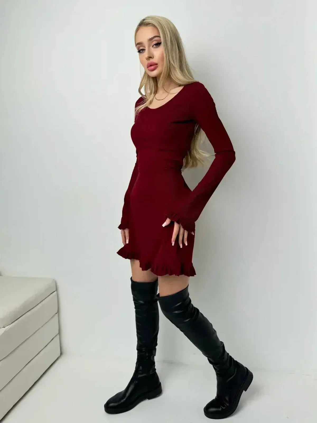 Model in a crimson red ribbed knit mini dress with ruffle hem and cuffs, paired with knee-high black boots.