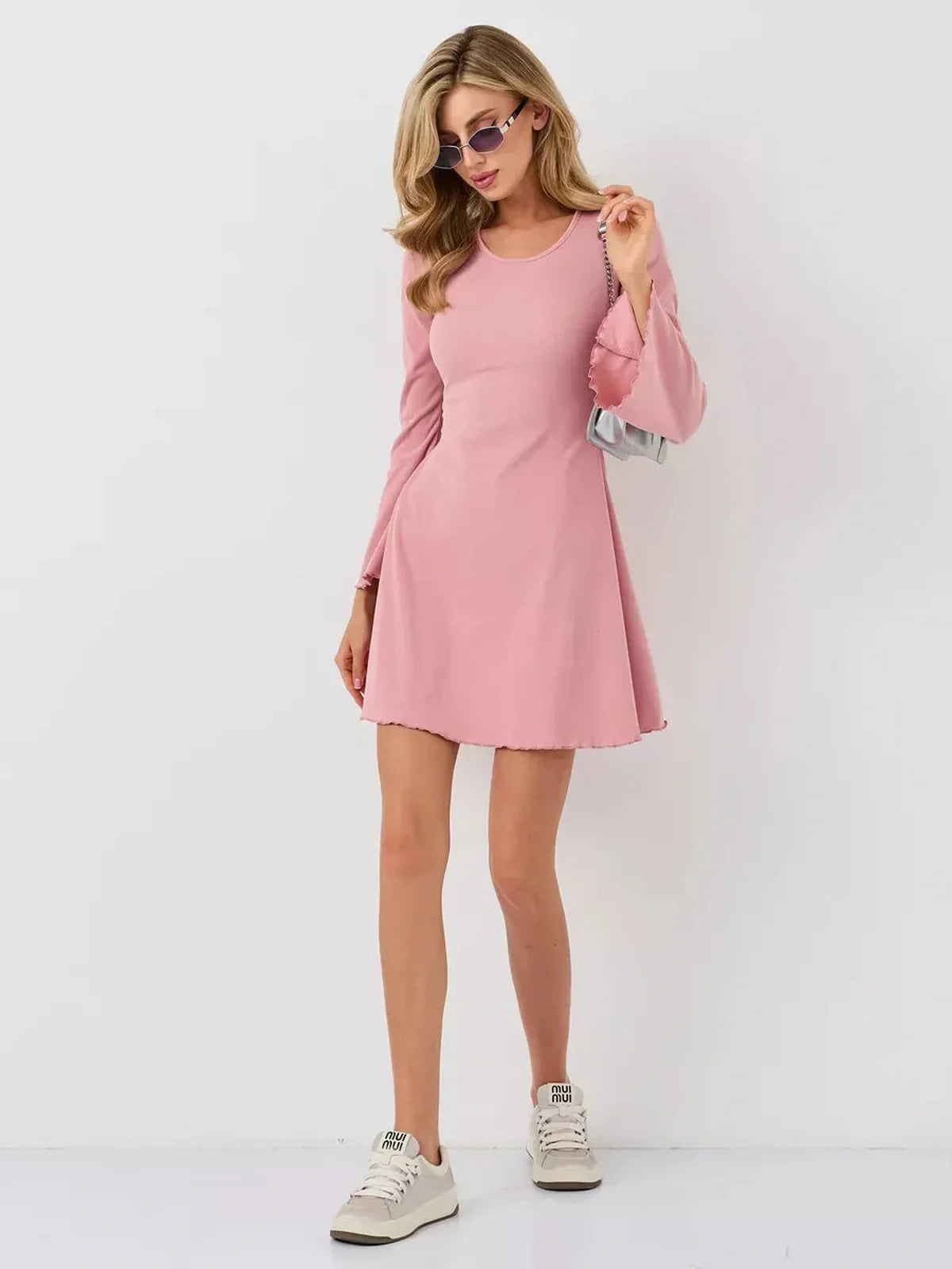 Model wearing a Blush Flare mini dress, featuring a soft pink hue, bell sleeves, and sporty sneakers.