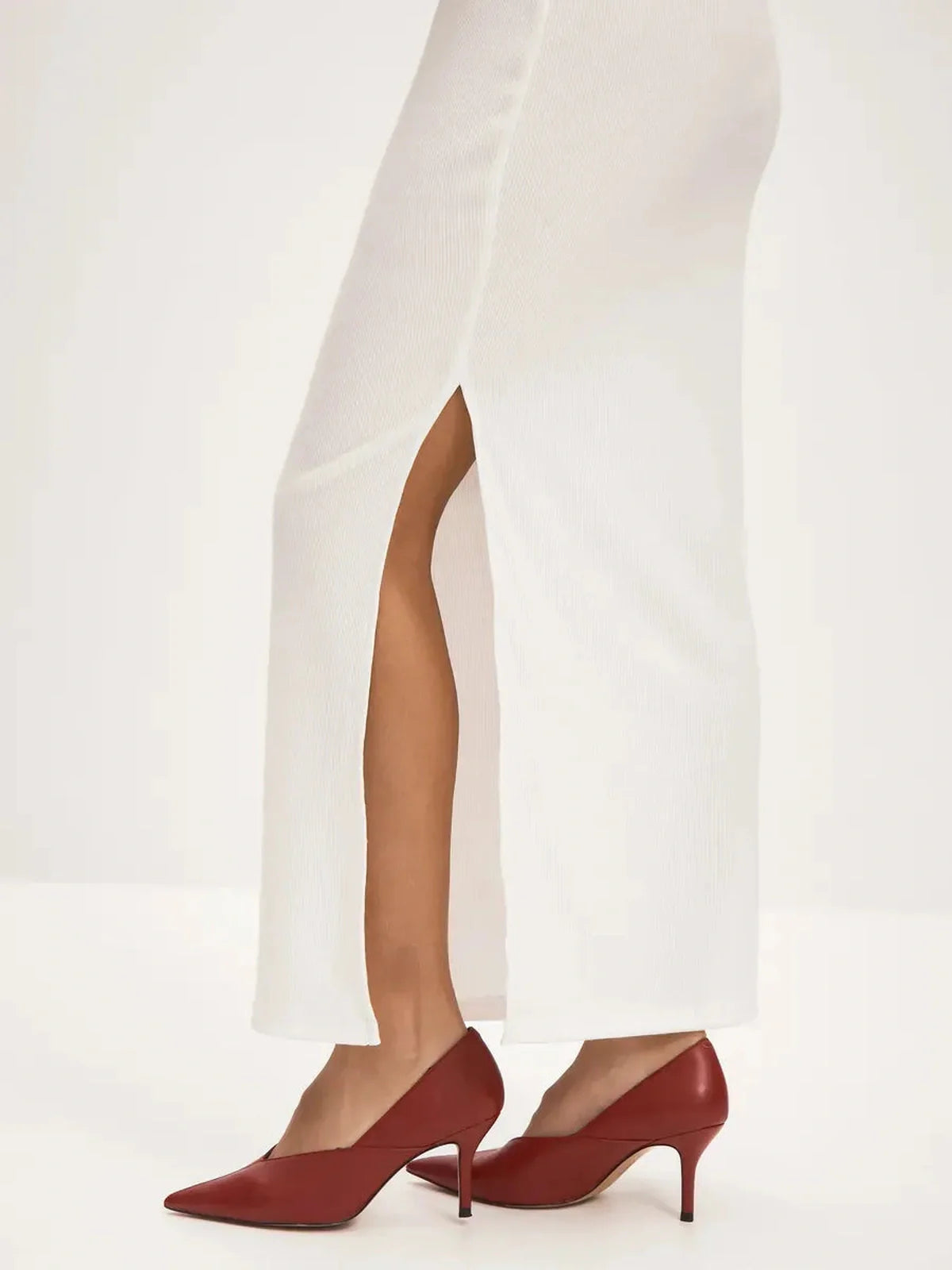 Off-shoulder white maxi dress with side slit, paired with elegant red high-heeled shoes.