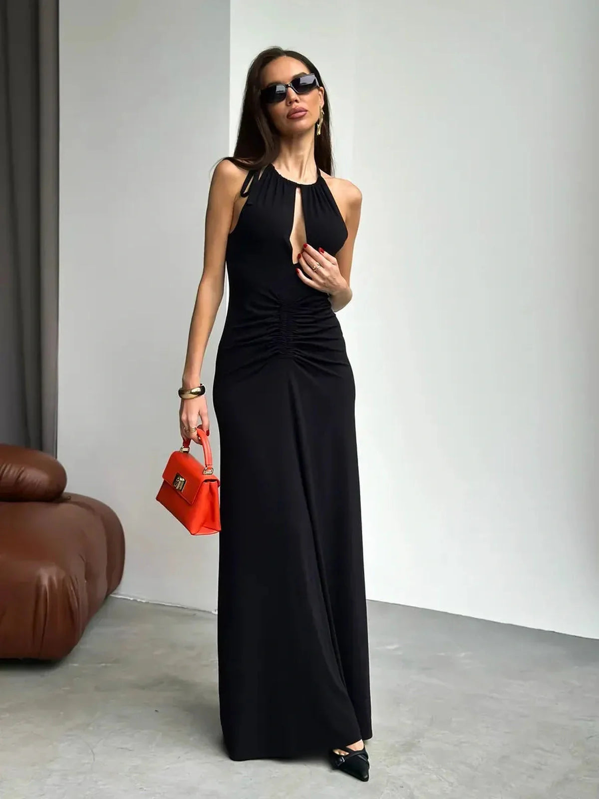 Elegant black maxi dress with ruched halter design, front slit, and stylish accessories for a chic summer look.
