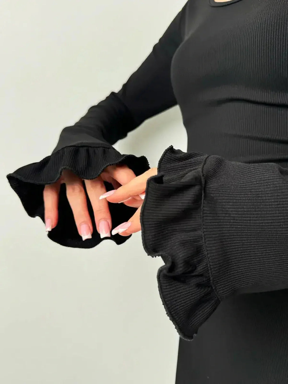 Close-up of model's hands in ruffled sleeves of a black Velvet Lace Mini dress showcasing the textured fabric.