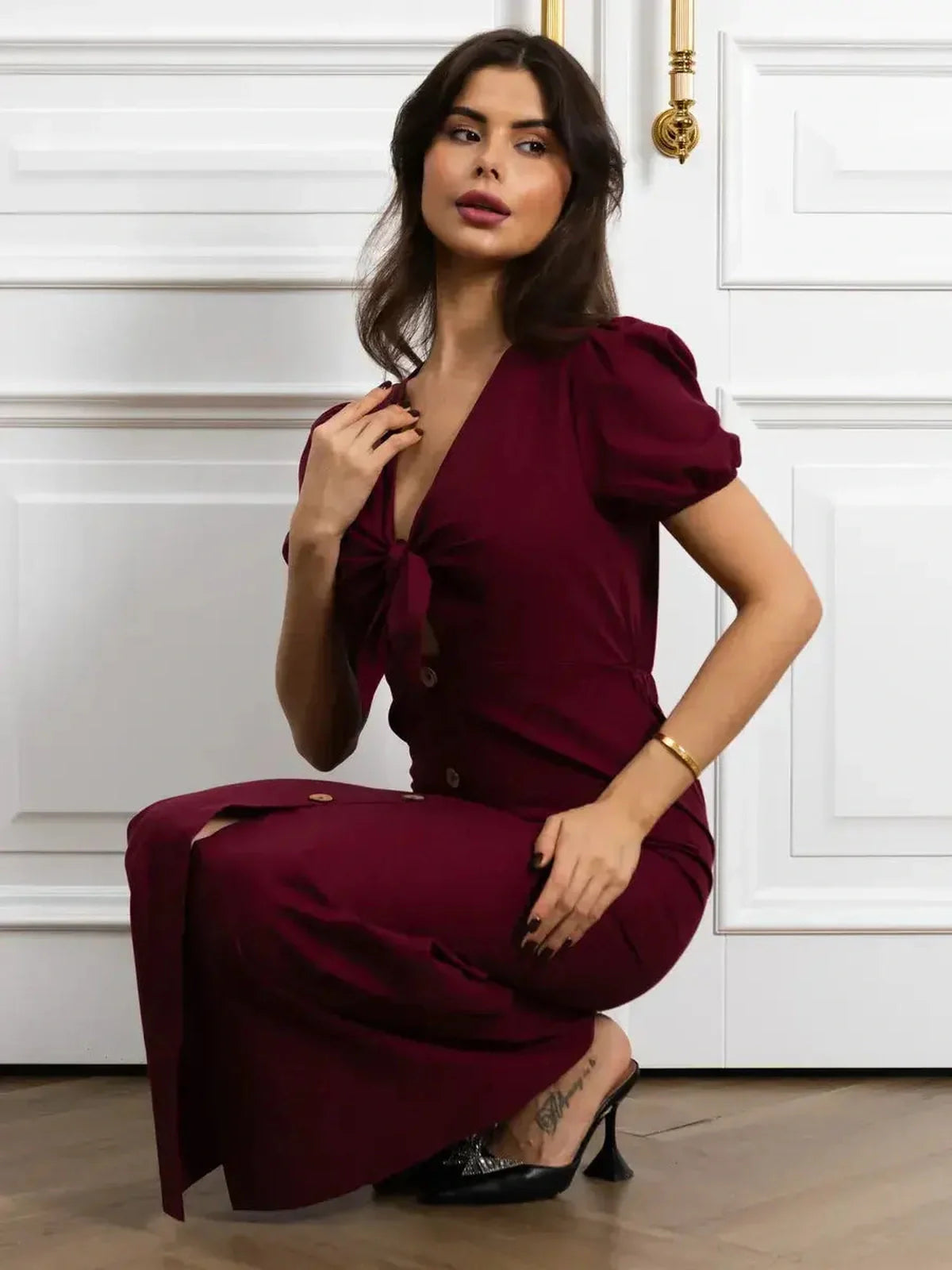 Model wearing a burgundy maxi dress with front bow, button detail, and puff sleeves, showcasing elegant fit and style.