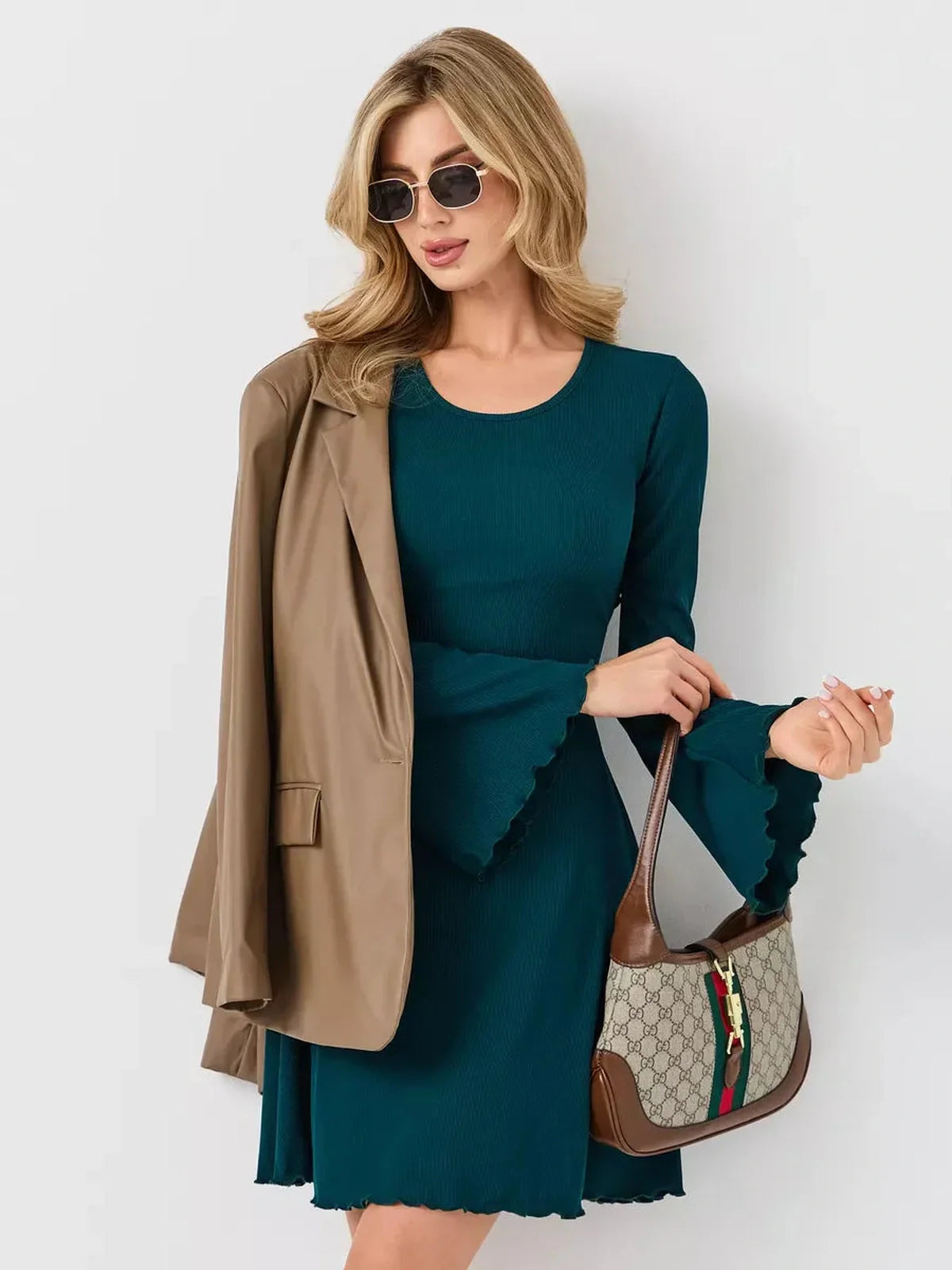 Woman in emerald green mini dress with ruffled sleeves, accessorized with sunglasses and a stylish bag.