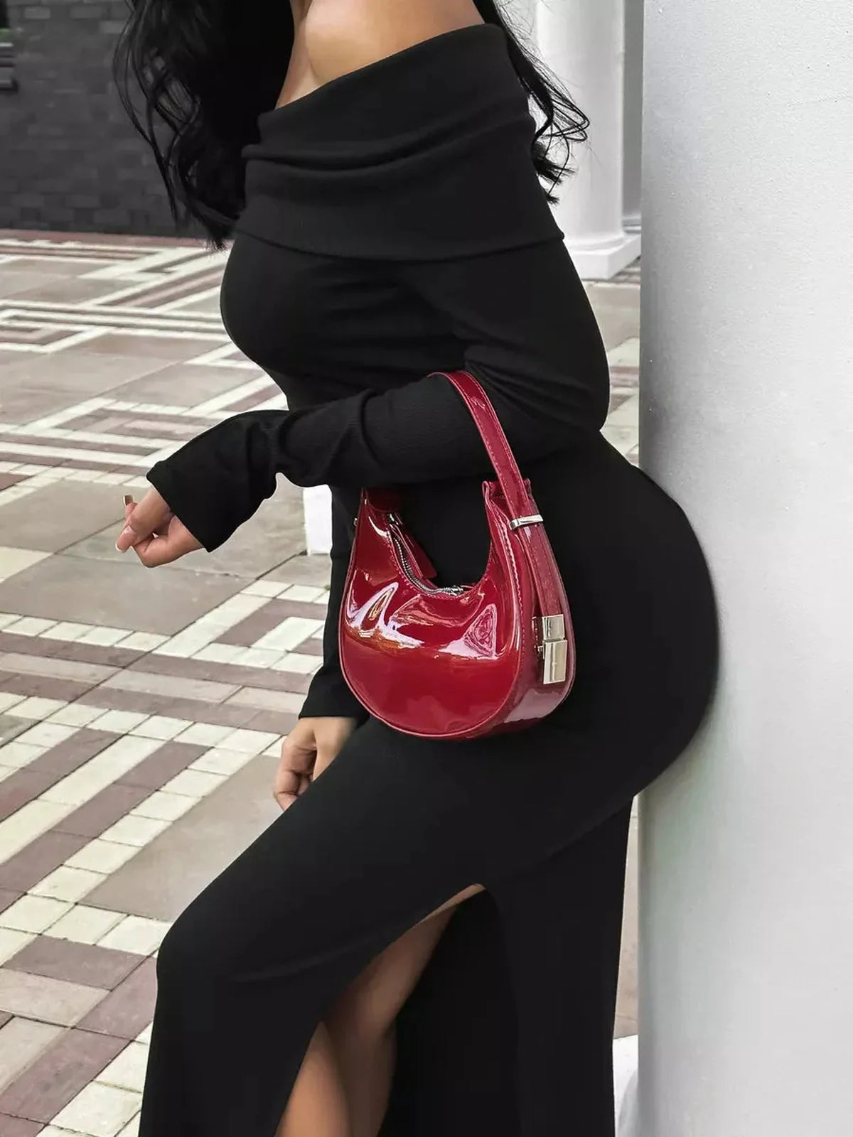 Iconic off-shoulder black maxi dress with flattering side slit, complemented by a stylish red handbag.