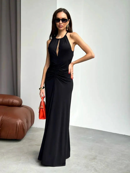 Elegant black maxi dress with ruched halter design, front slit, and stylish sunglasses, perfect for evening wear.