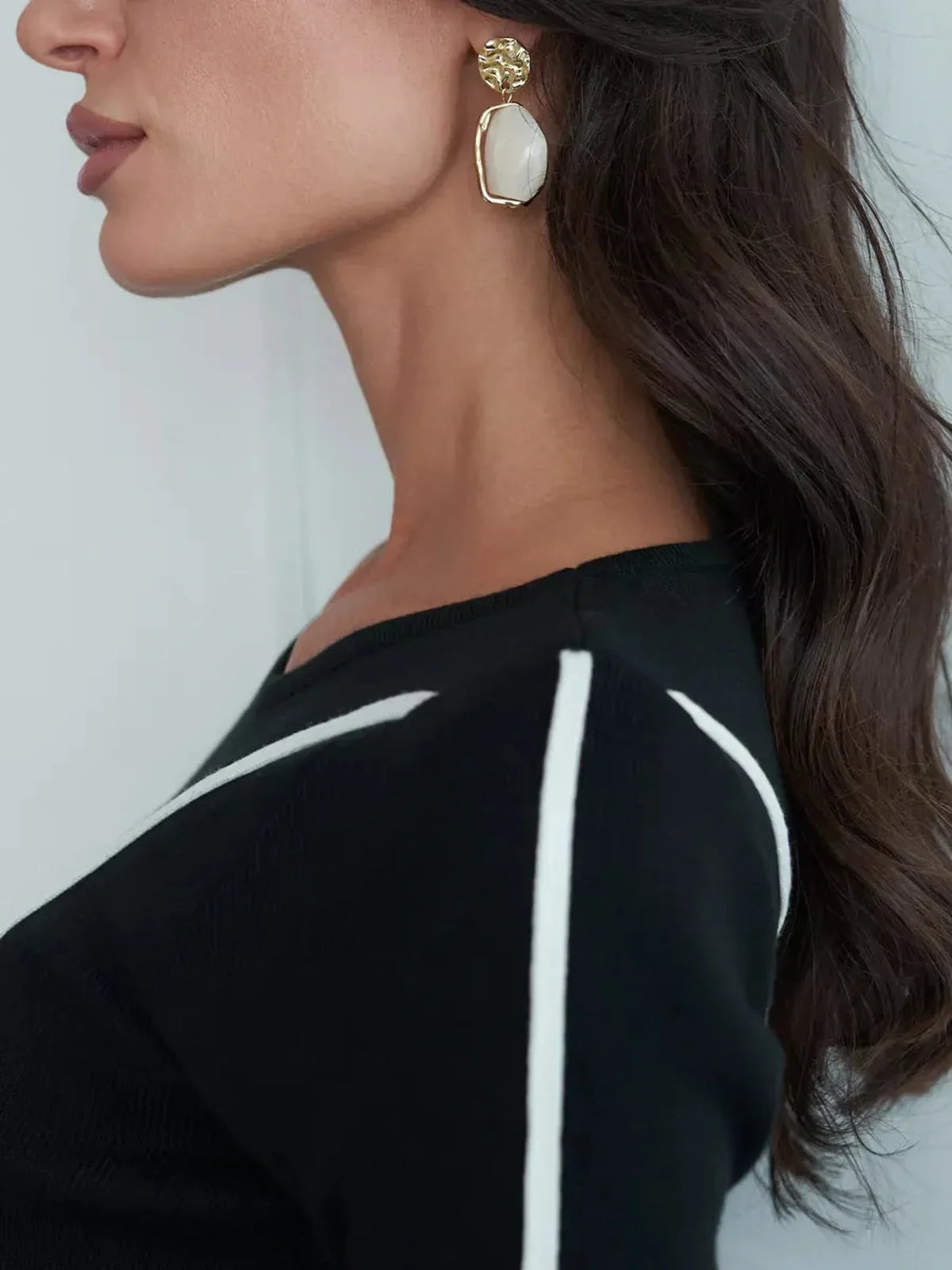 Close-up of a woman wearing a black dress with white piping and elegant earrings against a soft background.