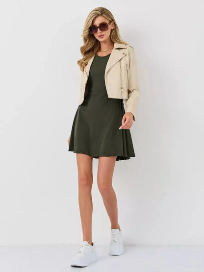 Model in an olive green mini dress with flared bell sleeves, paired with a cream jacket and stylish sunglasses.