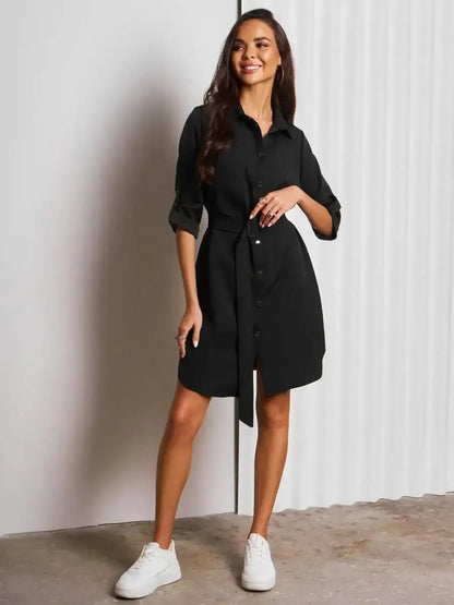 Model in a black Urban Edit Mini dress with structured silhouette and detachable belt, styled with white sneakers.