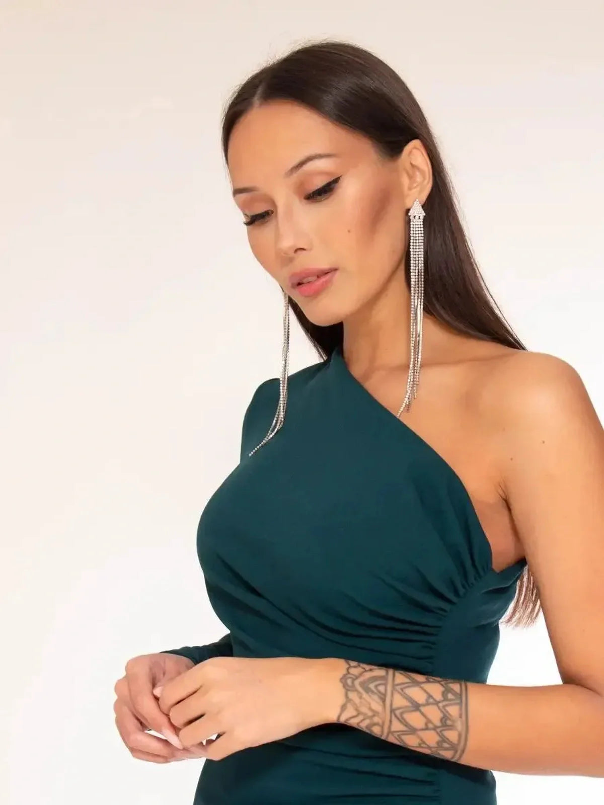 Model wearing a one-shoulder emerald green maxi dress with side slit and elegant accessories.