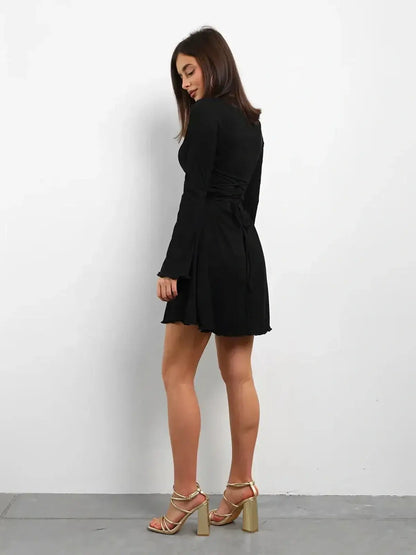 Woman wearing a black long sleeve mini dress with a lace-up back, perfect for cocktail parties or summer events.