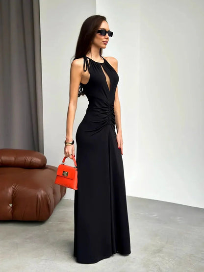 Elegant woman in a black maxi dress with ruched halter design and front slit, accessorized with a red handbag.