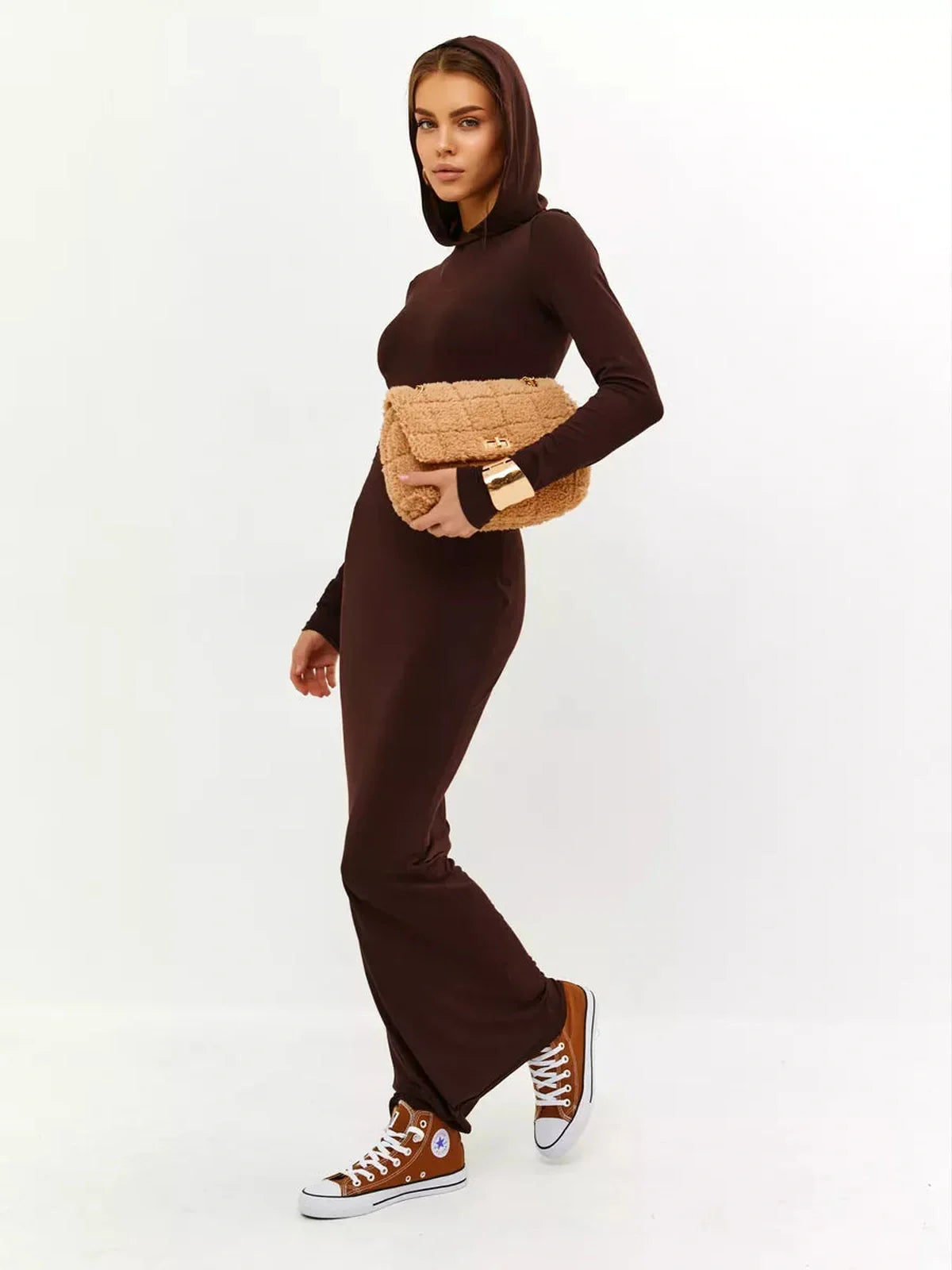 Woman in a brown hooded Sculpt Maxi Dress, styled with a clutch and sneakers, showcasing a sleek, elegant look.