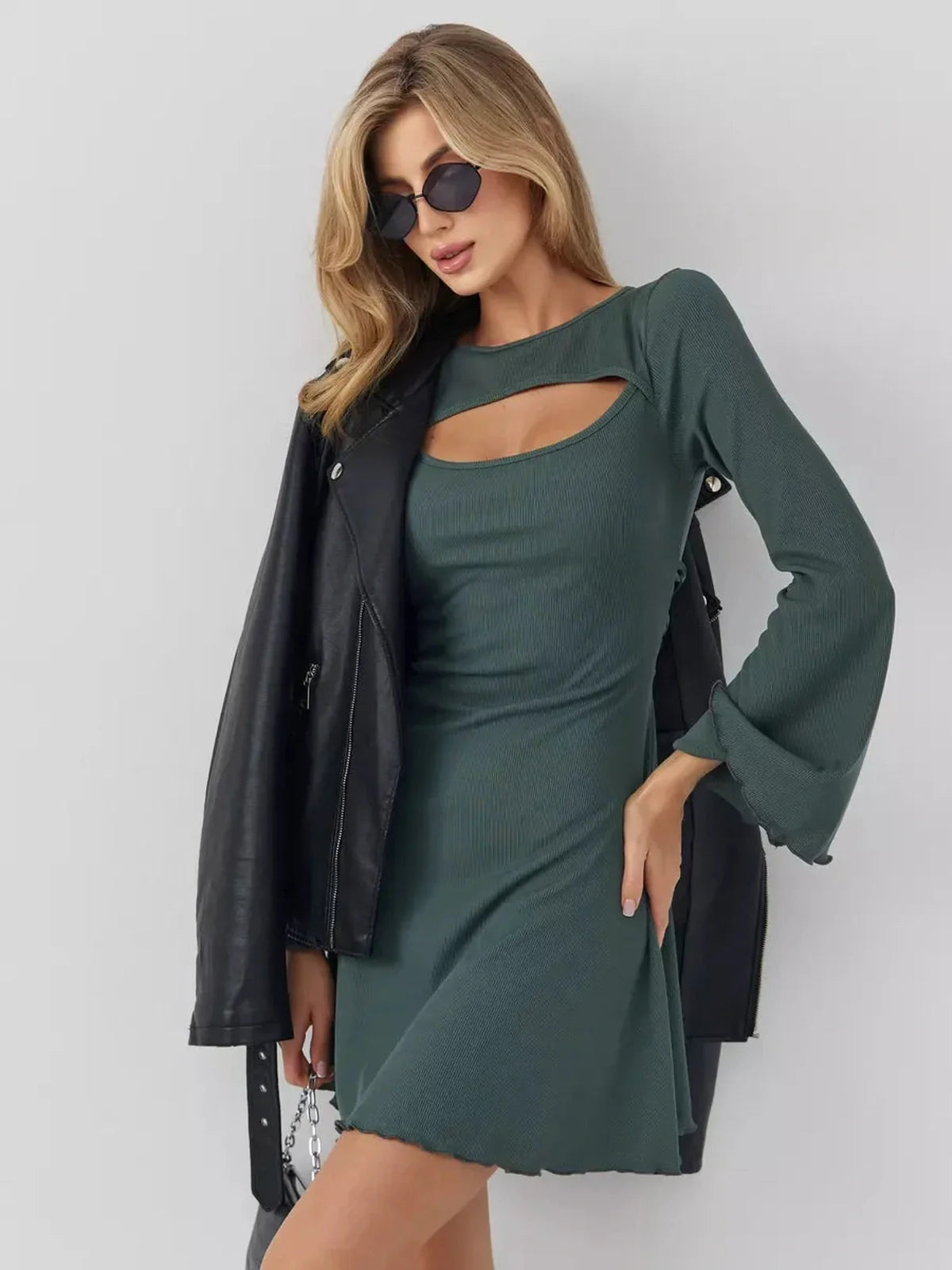 Model wearing a dark olive mini dress with bell sleeves and cut-out neckline, paired with a leather jacket and sunglasses.