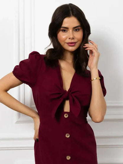 Model wearing a burgundy Maxi Dress Merlot Grace featuring a front tie bow and puff sleeves.