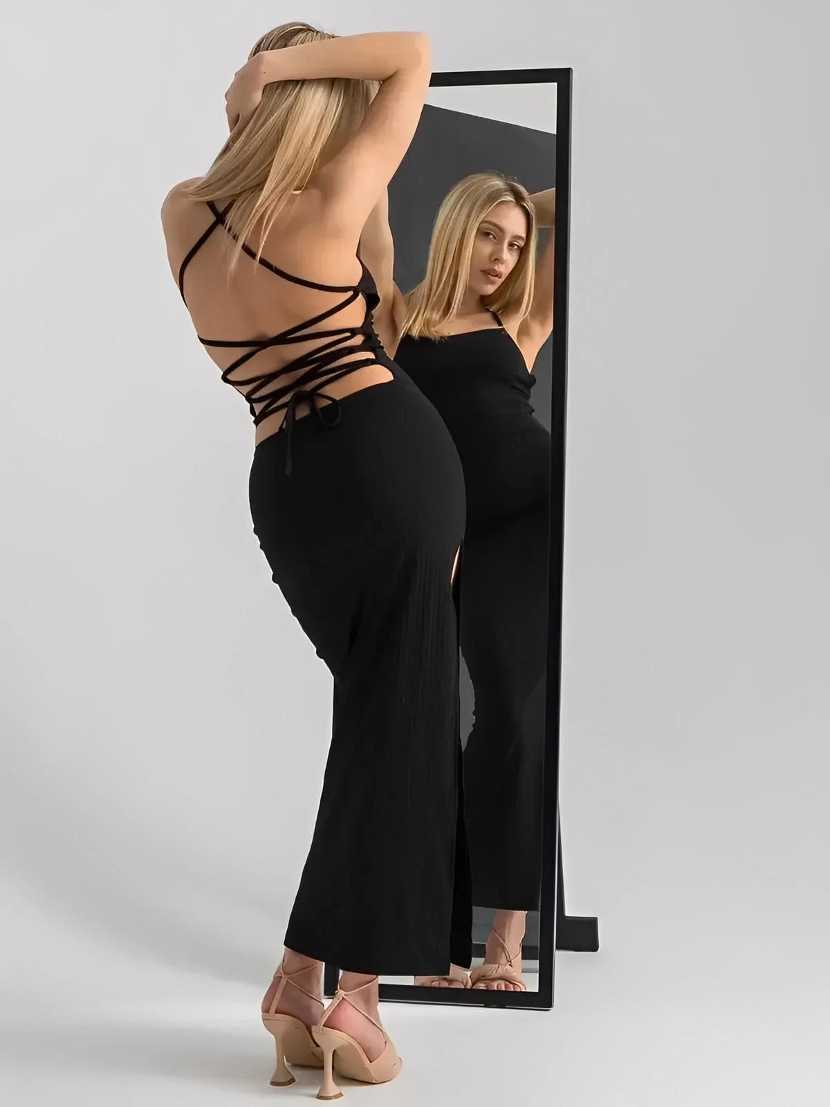 Model showcasing a Noir Lace Midi Dress with a lace-up back and thigh-high slit in front of a mirror.