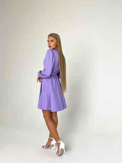 Elegant woman in a lilac mini dress with long sleeves, showcasing a cinched waist and stylish heels.