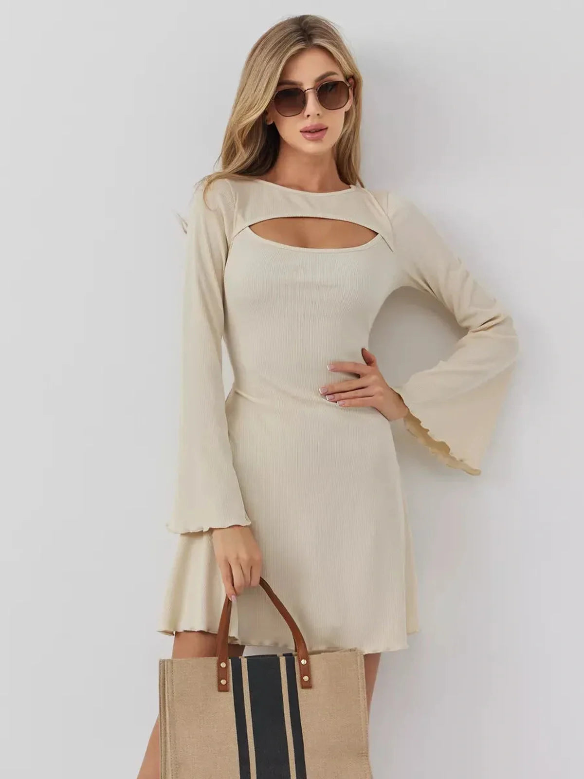 Model showcasing the Sculpted Grace mini dress with a boat neckline and front cutout, styled with a tote bag.
