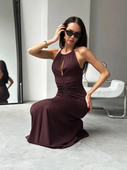 Model wearing a sleek Maxi Dress Sienna in rich sienna hue, showcasing halter neckline and ruched design.