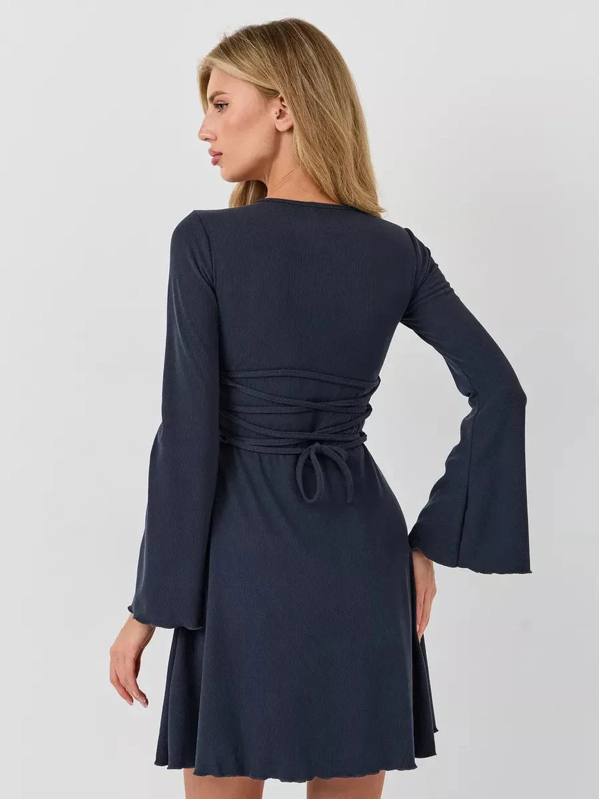 Model showcasing the elegant Graphite Grace mini dress with a lace-up back tie and bell sleeves.