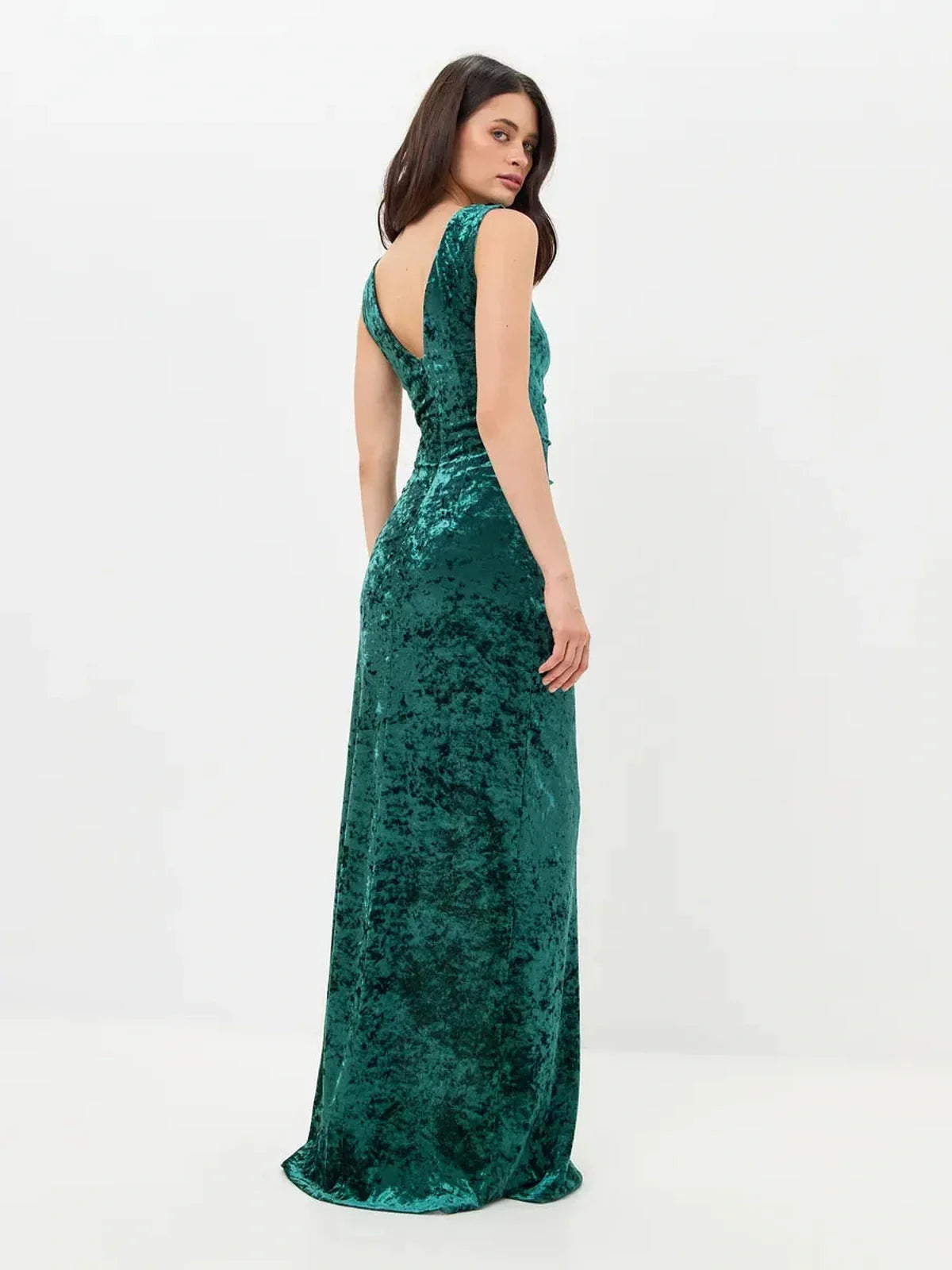 Elegant woman in a green velvet maxi dress showcasing a back slit and deep-V back design for formal occasions.