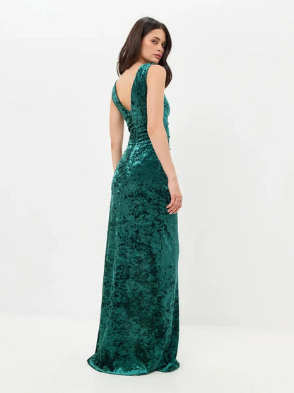 Elegant woman in a green velvet maxi dress showcasing a back slit and deep-V back design for formal occasions.