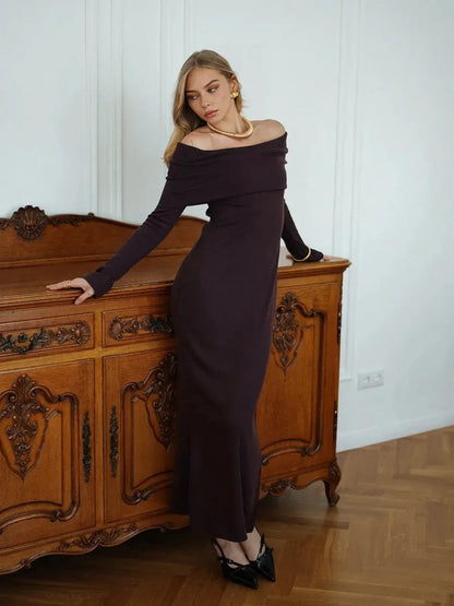 Elegance Maxi Dress in dark purple, featuring an off-shoulder design and ribbed texture, styled with chic black heels.