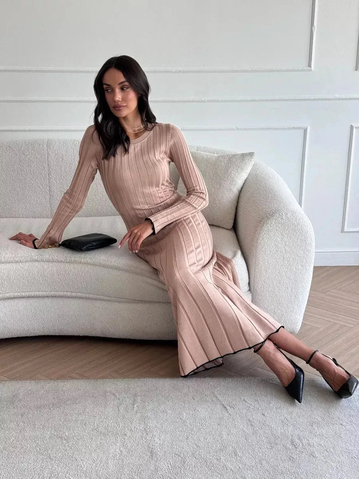 Model sitting gracefully on a sofa in a Sahara Curve Maxi Dress, showcasing its elegant ribbed design in sandstone beige.
