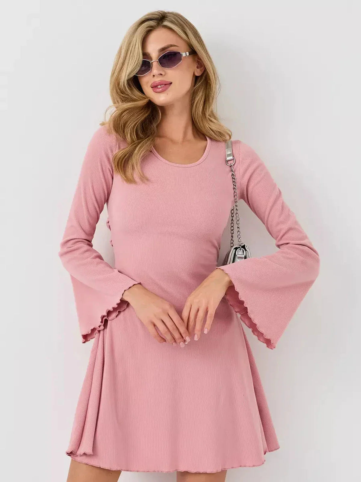 Model wearing the Blush Flare mini dress in soft pink, showcasing bell sleeves and a flared silhouette.