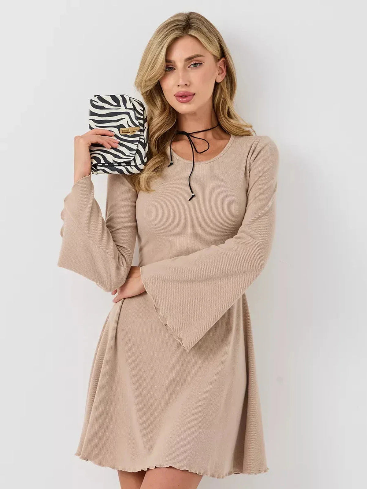 Model wearing a warm beige ribbed mini dress with bell sleeves, holding a zebra-print purse, showcasing a summer look.