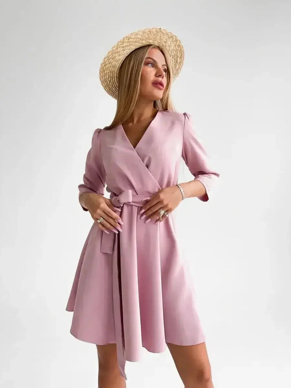 Model showcases the Rosé Flair pink mini dress with a V-neckline, long sleeves, and a removable belt, exuding elegance.
